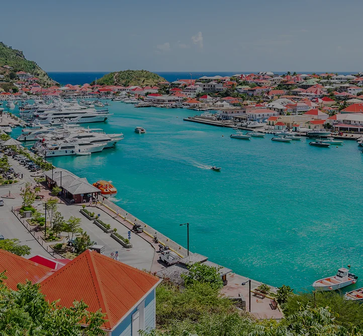 Stunning aerial view of St. Barts harbor with luxury yachts, red-roofed villas, and turquoise waters