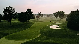 Pristine golf course at dawn with rolling fairways, sand bunkers, and morning mist over greens