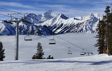 Snow-covered ski slopes with chairlift and dramatic mountain peaks under blue sky at alpine resort