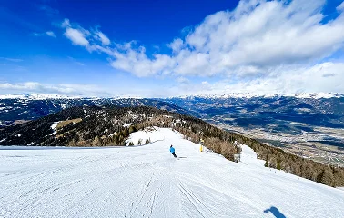 Skier descending pristine powder slopes with panoramic mountain views and blue skies at Vail resort