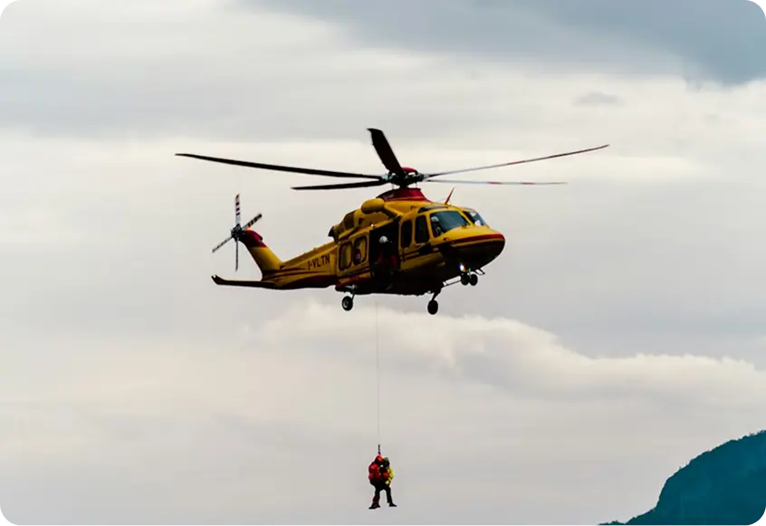 Yellow rescue helicopter hovering with a crew member on a winch line, illustrating Jetbay SOS emergency support